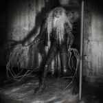  1boy absurdres body_horror cinemamind curly_hair design_speculation distortion_(tma) door doorway greyscale grin highres horror_(theme) jacket long_fingers long_hair male_focus michael_shelley monochrome monster monster_boy open_door painterly pants realistic shirt shoes smile standing teeth the_magnus_archives 