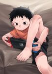  1boy absurdres barefoot black_eyes black_hair black_shorts child closed_mouth commentary commentary_request controller couch game_controller handheld_game_console highres indoors male_child male_focus nintendo_switch on_couch orange_shirt original shirt short_hair short_sleeves shorts sitting solo toes zumimi_mimi 