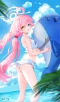  1girl bikini blue_archive blurry blurry_foreground blush breasts commentary depth_of_field floating_hair frilled_bikini frills halo heterochromia highres hoshino_(blue_archive) hoshino_(swimsuit)_(blue_archive) inflatable_orca inflatable_toy looking_at_viewer looking_to_the_side outdoors palm_leaf pink_hair rity small_breasts smile solo swimsuit twintails wading white_bikini 