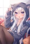  1girl :o animal_ears animal_hood arm_up bangs black_pantyhose blush breasts cat_ears cat_girl cat_hood cat_tail cleavage collarbone commentary_request day drawn_whiskers eyes_visible_through_hair fake_animal_ears fang feet_out_of_frame grey_hair grey_hoodie hair_between_eyes hair_ornament hair_over_shoulder hairclip hand_on_own_ear hand_up highres hood hood_up hoodie indoors knee_up long_hair long_sleeves looking_at_viewer no_pants open_mouth original pantyhose pillow puffy_long_sleeves puffy_sleeves purple_eyes ringouulu sidelocks sitting skin_fang sleeves_past_wrists solo tail tail_raised twitter_username white_hair window zipper 
