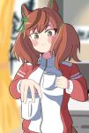  1girl animal_ears aoi_tenjiku blurry blurry_background blush bow brown_eyes closed_mouth coffee_mug commentary_request cup ear_bow ear_covers green_bow highres holding holding_cup horse_ears horse_girl horse_tail indoors jacket long_sleeves medium_hair mug nice_nature_(umamusume) red_hair red_jacket smile solo tail tracen_training_uniform track_jacket twintails umamusume 