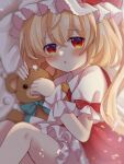  1girl ascot blonde_hair bloomers blush collared_shirt dorowa_(drawerslove) feet_out_of_frame flandre_scarlet frilled_pillow frills from_side hair_between_eyes hat highres holding holding_stuffed_toy indoors long_hair looking_at_viewer lying mob_cap on_bed on_side open_mouth pillow puffy_short_sleeves puffy_sleeves red_eyes red_vest shirt short_sleeves solo stuffed_animal stuffed_toy teddy_bear touhou underwear vest white_bloomers white_headwear white_shirt wrist_cuffs yellow_ascot 