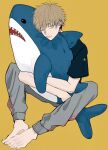  1boy barefoot blonde_hair chainsaw_man denji_(chainsaw_man) doll_hug grey_pants highres looking_at_viewer namida_a2 object_hug one_eye_closed pants shark short_hair simple_background solo track_pants yellow_background 