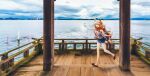  1girl animal_ear_fluff animal_ears bare_shoulders blue_shorts cellphone day denim denim_shorts fate/grand_order fate_(series) fishnet_top fishnets fox_ears fox_girl fox_tail full_body highres holding holding_phone lake long_hair looking_at_viewer official_art open_mouth orange_hair outdoors phone photo_background red_tank_top scenery short_shorts shorts sky slippers smartphone smile solo suzuka_gozen_(fate) suzuka_gozen_(under_the_same_sky)_(fate) tail takenoko_seijin tank_top water 
