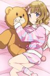  1girl ahoge bear_tail bed_sheet blue_eyes blush bow brown_hair commentary fake_tail hair_bow hug idolmaster idolmaster_million_live! idolmaster_million_live!_theater_days koma_tori long_sleeves looking_at_viewer lying medium_hair official_alternate_costume on_bed pajamas pink_bow pink_pajamas pink_shorts pink_socks shorts sidelocks signature smile socks solo stuffed_animal stuffed_toy suou_momoko tail teddy_bear wavy_hair 