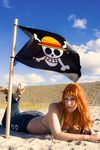  1girl beach bikini_top bracelet cosplay denim female flag highres jeans jewelry jolly_roger lying nami nami_(cosplay) nami_(one_piece) nami_(one_piece)_(cosplay) one_piece orange_hair outdoors pants photo pirate_flag real sand sandals sky solo 