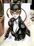  1girl animal_ears art_tools_in_frame artist's_hand_in_frame breasts catsuit catwoman cleavage closed_mouth collarbone commentary cropped_torso dc_comics english_commentary fake_animal_ears goggles highres holding holding_whip leather_suit marker_(medium) medium_breasts orange_outline outline photo_(medium) signature smile solo stanley_lau traditional_media whip 