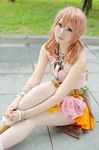  belt boots bracelet cosplay female final_fantasy final_fantasy_xiii grass jewelry looking_at_viewer midriff necklace oerba_dia_vanille oerba_dia_vanille_(cosplay) on_floor outdoors pink_shirt shirt sitting skirt solo tile tiles twintails 
