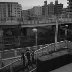  1girl 2boys absurdres apartment bridge building commentary_request gakuran greyscale highres kanagawa_prefecture lamppost long_hair miniskirt monochrome multiple_boys narue original overhead_line pedestrian_bridge photo_background railroad_tracks school_uniform short_hair skirt sweater wide_shot yokohama 