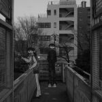  1boy 1girl absurdres apartment buttons commentary_request gakuran greyscale highres long_sleeves miniskirt monochrome narue open_mouth original outdoors photo_background pointing school_uniform shoes short_hair skirt smile sneakers socks standing sweater_vest tree 