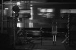  1girl absurdres arms_at_sides backpack bag commentary_request facing_away from_behind greyscale highres long_hair miniskirt monochrome motion_blur narue night original outdoors photo_background skirt socks solo standing sweater train wide_shot 