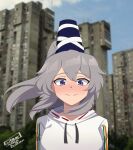  1girl adapted_costume blue_eyes blue_hat blurry blurry_background blush building closed_mouth commentary contemporary english_commentary grey_hair hat highres julian_belkan long_hair looking_at_viewer mononobe_no_futo outdoors ponytail signature skyscraper smile solo tate_eboshi touhou upper_body 