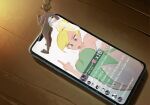  1girl bare_shoulders blonde_hair blue_eyes cellphone commentary dress english_commentary english_text fairy fairy_wings figures_taking_selfie_(meme) full_body green_dress hair_bun highres meme middle_finger mini_person minigirl philtomato phone pointy_ears short_hair single_hair_bun smartphone strapless strapless_dress tinker_bell_(disney) tongue tongue_out walt_disney's_peter_pan wings 
