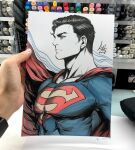  1boy art_tools_in_frame artist's_hand_in_frame black_hair blue_bodysuit bodysuit cape clark_kent closed_mouth commentary dc_comics english_commentary highres male_focus marker_(medium) muscular muscular_male photo_(medium) red_cape serious short_hair signature solo stanley_lau superhero_costume superman superman_(series) superman_logo traditional_media upper_body 