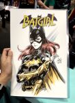  1girl artist's_hand_in_frame barbara_gordon batarang batgirl batgirl_costume_(2011) batman_(series) belt black_bodysuit black_cape bodysuit breasts cape closed_mouth commentary cowl dc_comics english_commentary gloves highres holding holding_weapon long_hair looking_at_viewer marker_(medium) photo_(medium) red_hair signature stanley_lau traditional_media upper_body utility_belt weapon yellow_cape yellow_gloves 