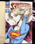  1girl blonde_hair blue_eyes blue_shirt breasts cape closed_mouth commentary cover_sketch dc_comics english_commentary highres long_hair long_sleeves looking_at_viewer marker_(medium) photo_(medium) red_cape shirt signature smile solo stanley_lau supergirl superman_(series) traditional_media upper_body 
