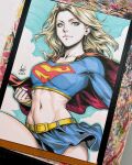  1girl belt blonde_hair blue_eyes blue_shirt blue_skirt breasts cape clenched_hand commentary crop_top dc_comics english_commentary highres long_hair long_sleeves marker_(medium) photo_(medium) red_cape shirt signature skirt solo stanley_lau supergirl superman_(series) superman_logo traditional_media 