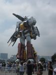  blurry cannon cloud cloudy_sky depth_of_field gundam kou_(mechalog) looking_at_viewer mecha no_humans outdoors perfect_gundam plamo-kyo_shiro realistic size_difference sky solo standing taking_picture yellow_eyes 