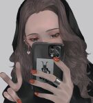  1girl aegyo_sal black_eyes black_hoodie brown_hair card cellphone commentary_request ear_chain earrings eyeshadow grey_background heart heart_earrings highres holding holding_phone hood hood_up hoodie jewelry linked_piercing long_hair looking_at_phone makeup mano_aaa mole mole_under_eye nail_polish original phone phone_over_face piercing red_nails ring selfie simple_background sleeves_past_wrists smartphone solo tarot tarot_card 