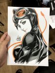  1girl art_tools_in_frame artist's_hand_in_frame batman_(series) black_bodysuit black_hair bodysuit breasts catsuit catwoman closed_mouth commentary cropped_torso dc_comics english_commentary goggles goggles_on_head green_eyes highres looking_at_viewer marker_(medium) orange_outline outline photo_(medium) signature solo stanley_lau traditional_media white_background 