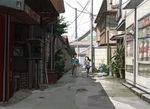  1girl alley black_hair building child city house long_hair original outdoors pavement payphone phone plant potted_plant power_lines saitama_(nrh49840) scenery shadow short_hair sign sunlight telephone_pole vanishing_point vending_machine walking 