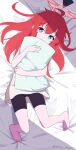  1girl ahoge barefoot bed_sheet bike_shorts blue_archive blue_eyes bright_pupils commentary_request halo highres holding holding_pillow long_hair looking_at_viewer lying maki_(blue_archive) millet_pepper on_back pillow red_hair red_halo shirt solo toes twitter_username white_pupils white_shirt 