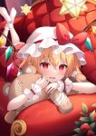  1girl black_eyeliner blonde_hair bow couch crystal cuffs dress eyelashes eyeliner flandre_scarlet flower frilled_cuffs frills hat hat_bow hat_ribbon highres hug looking_at_viewer lying makeup miy@ mob_cap on_stomach one_side_up open_mouth red_bow red_dress red_eyes red_flower red_rose ribbon rose short_hair side_ponytail smile solo stuffed_animal stuffed_toy teddy_bear touhou white_headwear wings wrist_cuffs 
