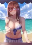  1girl beach bikini bikini_pull bikini_skirt blue_bikini blue_eyes blush breasts brown_hair cleavage closed_mouth clothes_pull collarbone day flashing frilled_bikini frills go-toubun_no_hanayome gomashiwo_o hair_between_eyes large_breasts leaning_forward long_hair looking_at_viewer nakano_miku navel ocean outdoors sky solo swimsuit 