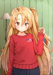  ame. american_flag azur_lane bangs blue_pants blush book brown_eyes casual cleveland_(azur_lane) closed_mouth commentary eyebrows_visible_through_hair hair_between_eyes indoors lamp light_brown_hair long_hair long_sleeves looking_at_viewer one_side_up pants red_sweater sleeves_past_wrists solo sweater very_long_hair 