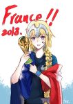  1girl 2018_fifa_world_cup alternate_costume bangs blonde_hair blue_eyes bracelet braid eyebrows_visible_through_hair fate/grand_order fate_(series) flag france french_flag hair_over_shoulder headpiece highres holding jeanne_d'arc_(fate) jeanne_d'arc_(fate)_(all) jewelry long_braid long_hair looking_at_viewer open_mouth simple_background single_braid smile soccer soccer_uniform solo sportswear text_focus trophy very_long_hair world_cup yano_senyuki 