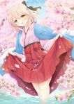  1girl ahoge bangs black_ribbon blonde_hair blue_sky blush cherry_blossoms commentary_request eyebrows_visible_through_hair falling_petals fate_(series) hair_between_eyes hair_ribbon hakama half_updo in_water iris_yayoi japanese_clothes kimono lifted_by_self looking_at_viewer okita_souji_(fate) okita_souji_(fate)_(all) outdoors ribbon short_hair sidelocks skirt skirt_lift sky smile solo standing water yellow_eyes 