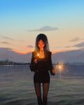  1girl black_coat black_dress black_hair black_pantyhose city_lights closed_eyes coat collar dress feet_out_of_frame fireworks highres holding holding_fireworks long_hair looking_at_object mountainous_horizon original pantyhose reflection reflective_water sam_yang short_dress skyline smile solo sparkler sunset 