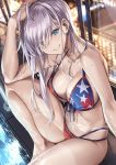  1girl american_flag_bikini bangs bare_shoulders bikini blue_eyes blurry blurry_background blush bokeh breasts city_lights cleavage closed_mouth collarbone depth_of_field elbow_on_knee eyebrows_visible_through_hair fate/grand_order fate_(series) flag_print hand_on_own_head head_tilt highres indoors knee_up ks large_breasts long_hair looking_at_viewer miyamoto_musashi_(fate/grand_order) miyamoto_musashi_(swimsuit_berserker)_(fate) multi-strapped_bikini navel night pink_hair poolside sandals sidelocks sitting skindentation smile solo sparkle stomach swept_bangs swimsuit tan tanline thighs wet window 