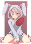  1girl animal_ears azur_lane bangs blush bunny_ears embarrassed eyebrows_visible_through_hair falsche.shido hair_ornament highres holding holding_torpedo hood hoodie long_sleeves looking_at_viewer platinum_blonde_hair purple_eyes short_hair smile solo spread_legs sweatdrop torpedo z23_(azur_lane) 