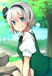  1girl bangs black_neckwear blue_eyes blush bob_cut breasts day green_vest grin hair_between_eyes hairband highres katsuobushi_(eba_games) konpaku_youmu outdoors rock shirt short_hair short_sleeves silver_hair small_breasts smile solo touhou tree vest white_shirt 