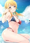  1girl ahoge american_flag_bikini ass bangs bikini blonde_hair blue_eyes blue_nails blue_sky blush bracelet collarbone commentary day flag_print grin hachimiya_meguru highres idolmaster idolmaster_shiny_colors jewelry lens_flare long_hair looking_at_viewer low_twintails nail_polish navel ocean outdoors sky smile solo swimsuit twintails v yellow_nails yuzuyu_(hyui) 