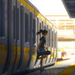  1girl artist_logo black_shirt blue_shorts blurry blurry_background blurry_foreground brown_hair bysau commentary day depth_of_field english_commentary grey_footwear ground_vehicle highres holding instrument_case jun_(bysau) medium_hair original outdoors ponytail shade shirt shoes short_sleeves shorts sneakers solo standing t-shirt train train_station walking white_sky 