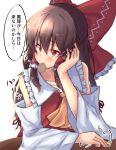  1girl absurdres ascot blush bow brown_hair collarbone commentary_request detached_sleeves eyebrows_visible_through_hair food_in_mouth frilled_bow frilled_shirt_collar frills hair_bow hair_tubes hakurei_reimu head_rest highres mukkushi red_eyes simple_background solo tapping touhou translation_request upper_body white_background yellow_neckwear 