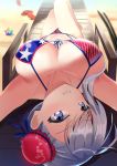  1girl absurdres american_flag_bikini asymmetrical_hair bangs bare_shoulders bikini blue_eyes blush boo_iro breasts bun_cover cleavage closed_mouth collarbone fate/grand_order fate_(series) flag_print grey_hair hair_bun highres large_breasts long_hair looking_at_viewer lying miyamoto_musashi_(fate/grand_order) miyamoto_musashi_(swimsuit_berserker)_(fate) navel on_back saint_quartz sandals side_bun smile swept_bangs swimsuit thighs upside-down 