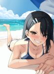  1girl bare_shoulders beach beach_umbrella bikini black_hair blue_bikini blue_sky blush breasts brown_eyes cleavage cloud collarbone commentary_request ear_clip eyes_visible_through_hair fangs foot_up grin hair_ornament hairclip highres ijiranaide_nagatoro-san junkt729 leg_up long_hair looking_at_viewer lying medium_breasts nagatoro_hayase nose_blush ocean on_stomach one-piece_tan sand shadow sky smile solo swimsuit tan tanline teeth umbrella water wet wet_hair 