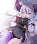  1girl absurdres bare_shoulders belt blush braid fang hair_between_eyes highres hololive horns la+_darknesss long_hair lying nintendo_switch on_back open_mouth pillow pointy_ears purple_hair purple_legwear silver_hair single_thighhigh solo thighhighs utsusumi_kio very_long_hair virtual_youtuber yellow_eyes 