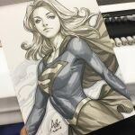  1girl art_tools_in_frame blonde_hair blue_eyes blue_shirt breasts cape commentary dc_comics english_commentary long_hair long_sleeves marker_(medium) photo_(medium) sepia shirt signature skirt solo stanley_lau supergirl superman_(series) superman_logo traditional_media 