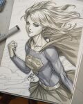 1girl art_tools_in_frame blonde_hair blue_shirt breasts cape closed_mouth commentary dc_comics english_commentary highres long_hair long_sleeves looking_at_viewer marker_(medium) photo_(medium) sepia shirt signature skirt smile stanley_lau supergirl superman_(series) superman_logo traditional_media 